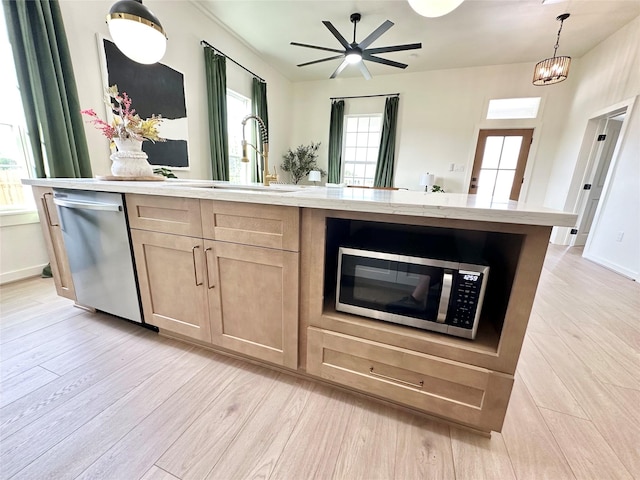 kitchen featuring appliances with stainless steel finishes, light brown cabinetry, light wood-type flooring, pendant lighting, and a sink