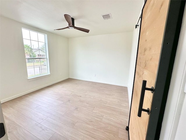 spare room with visible vents, a barn door, ceiling fan, light wood-type flooring, and baseboards