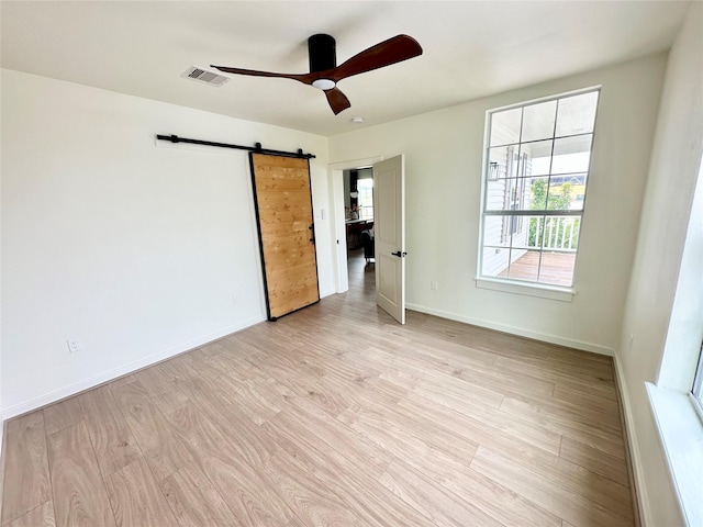 empty room featuring light wood finished floors, visible vents, a barn door, a ceiling fan, and baseboards