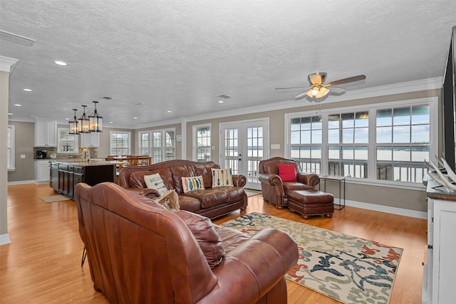 living room featuring ceiling fan with notable chandelier, light wood-type flooring, a textured ceiling, and ornamental molding