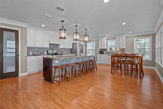 kitchen with white cabinets, appliances with stainless steel finishes, a center island with sink, and decorative light fixtures