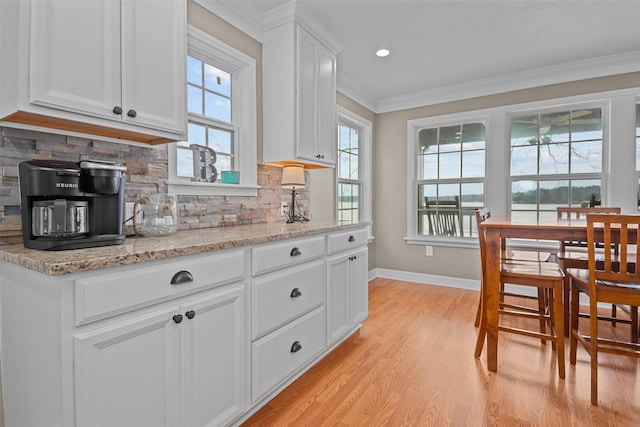 kitchen with white cabinets, crown molding, light wood-type flooring, tasteful backsplash, and light stone counters