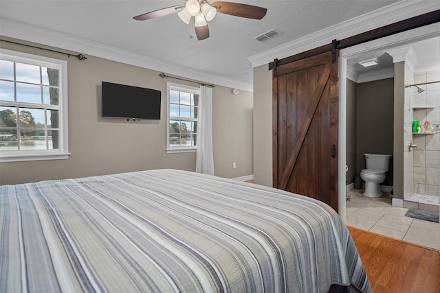 bedroom with ceiling fan, a barn door, crown molding, and ensuite bath