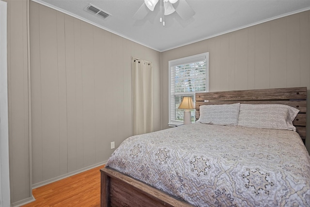 bedroom featuring light wood-type flooring, ceiling fan, ornamental molding, and wood walls