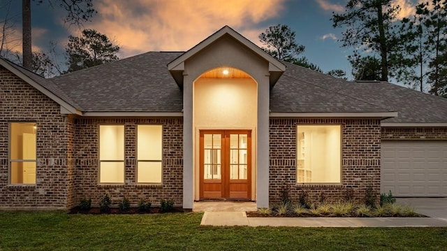 exterior entry at dusk with french doors, a garage, and a yard