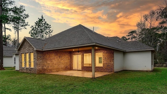 back house at dusk featuring a patio area and a lawn