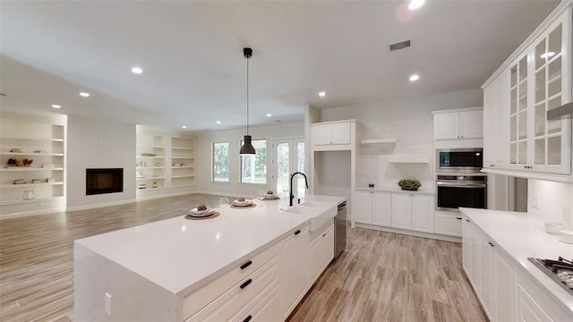 kitchen featuring sink, appliances with stainless steel finishes, an island with sink, white cabinets, and decorative light fixtures