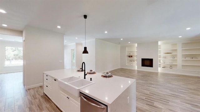 kitchen featuring sink, dishwasher, a kitchen island with sink, white cabinets, and decorative light fixtures