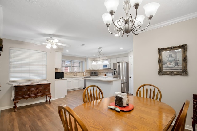 dining room featuring ceiling fan with notable chandelier, crown molding, sink, and light hardwood / wood-style flooring