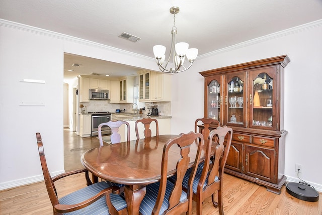 dining space with light hardwood / wood-style floors, ornamental molding, sink, and an inviting chandelier