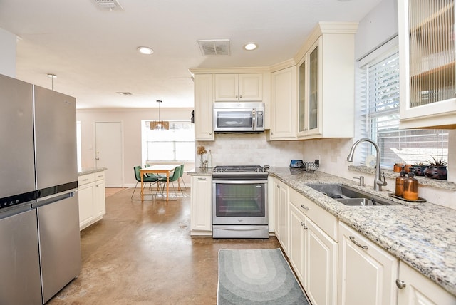 kitchen with light stone countertops, sink, hanging light fixtures, and appliances with stainless steel finishes