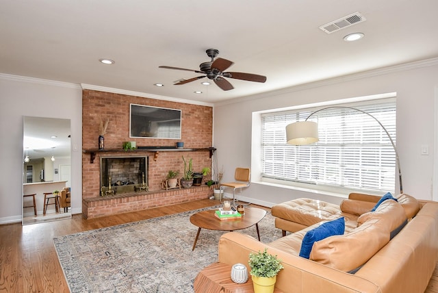 living room featuring ceiling fan, a fireplace, wood-type flooring, and ornamental molding