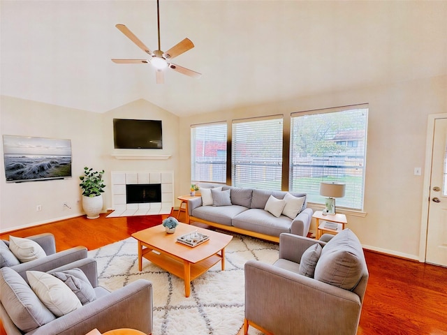 living room with ceiling fan, lofted ceiling, wood-type flooring, and a tiled fireplace