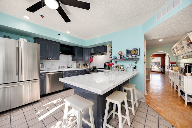 kitchen featuring ceiling fan, kitchen peninsula, a textured ceiling, a kitchen bar, and appliances with stainless steel finishes