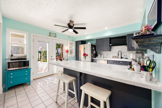 kitchen with french doors, a kitchen breakfast bar, ceiling fan, appliances with stainless steel finishes, and tasteful backsplash