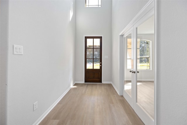 entryway with a high ceiling, light hardwood / wood-style flooring, a wealth of natural light, and french doors