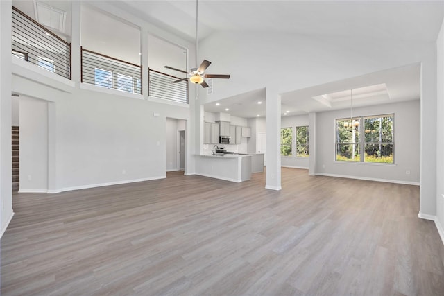 unfurnished living room featuring ceiling fan with notable chandelier, light hardwood / wood-style floors, a towering ceiling, and sink