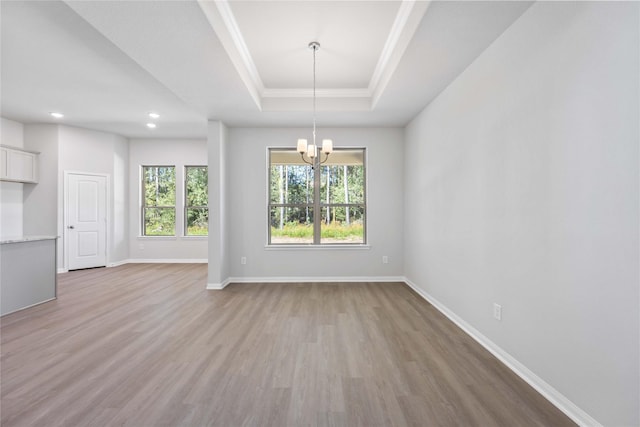 unfurnished dining area featuring light hardwood / wood-style floors, a raised ceiling, and a chandelier