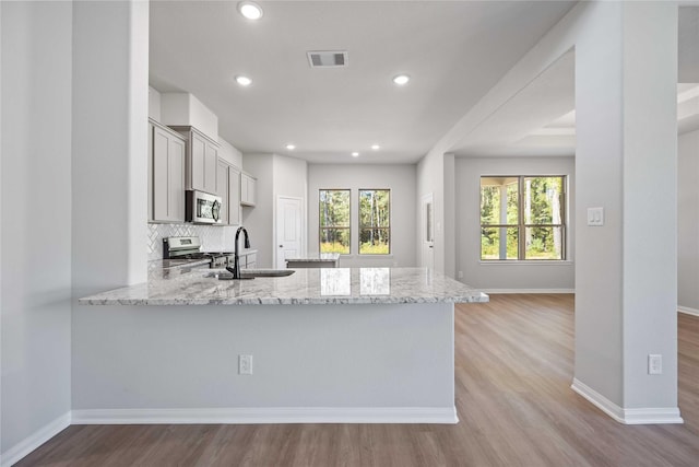 kitchen with sink, light wood-type flooring, light stone counters, kitchen peninsula, and stainless steel appliances