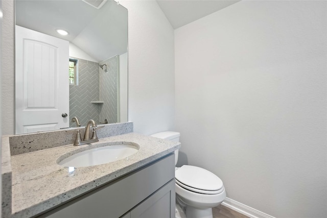 bathroom featuring tiled shower, vanity, toilet, and vaulted ceiling