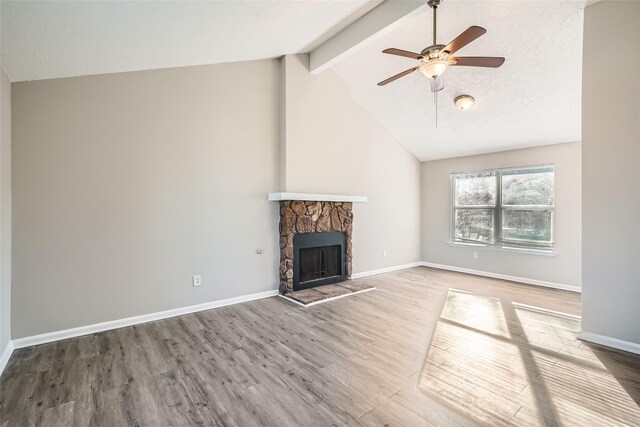 unfurnished living room featuring a stone fireplace, ceiling fan, hardwood / wood-style floors, and lofted ceiling with beams