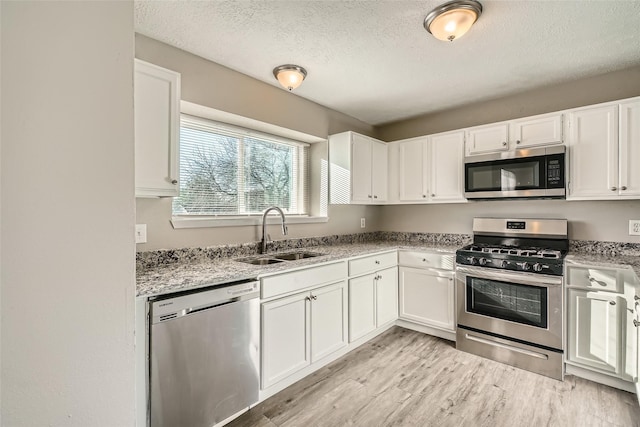 kitchen with light stone countertops, sink, stainless steel appliances, a textured ceiling, and white cabinets