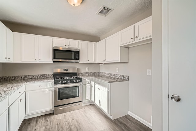 kitchen with light stone countertops, white cabinets, stainless steel appliances, and light hardwood / wood-style floors