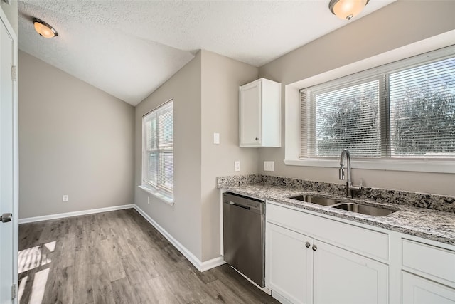 kitchen with lofted ceiling, white cabinets, sink, stainless steel dishwasher, and light stone countertops