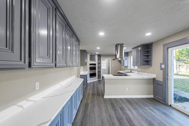 kitchen with kitchen peninsula, light stone countertops, island range hood, sink, and dark hardwood / wood-style floors