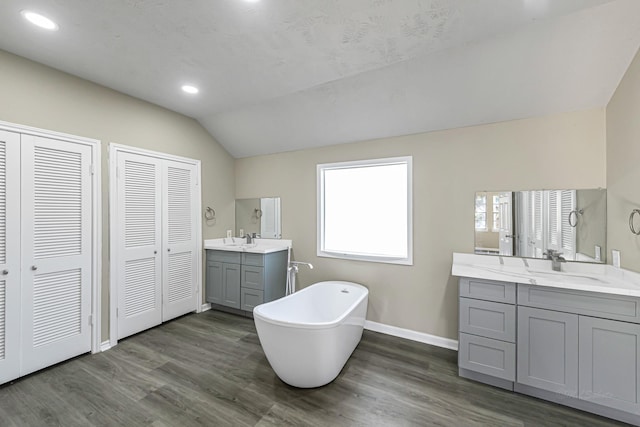 bathroom with a tub to relax in, hardwood / wood-style floors, vanity, and vaulted ceiling