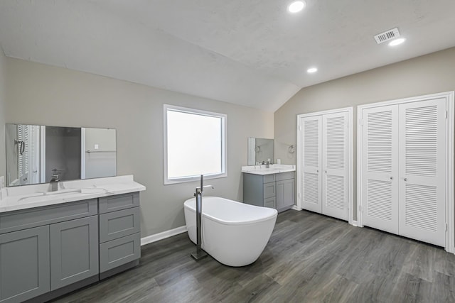 bathroom featuring wood-type flooring, vanity, vaulted ceiling, and a bathing tub