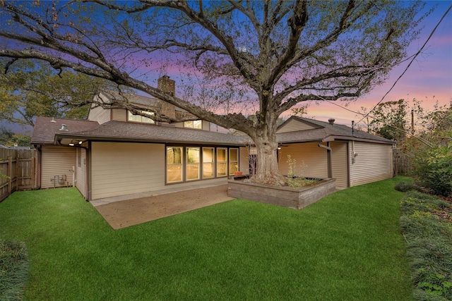 back house at dusk featuring a patio area and a lawn