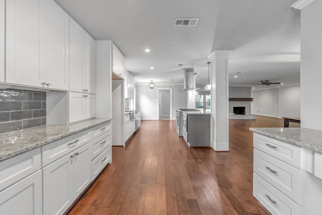 kitchen with white cabinets, a fireplace, stainless steel gas stove, ceiling fan, and island exhaust hood