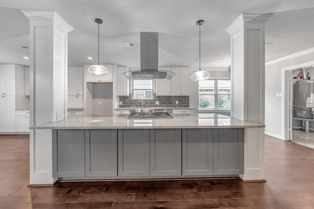 kitchen featuring island exhaust hood, light stone counters, white cabinets, decorative light fixtures, and decorative columns