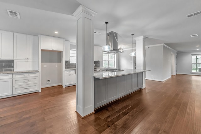 kitchen featuring light stone countertops, island range hood, white cabinetry, and pendant lighting