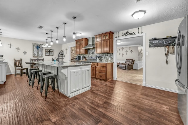 kitchen with pendant lighting, a center island with sink, decorative backsplash, stainless steel fridge, and a kitchen bar