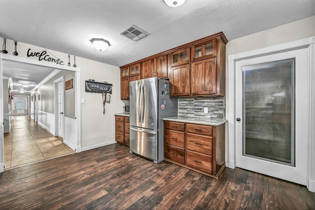 kitchen with decorative backsplash, light stone counters, a textured ceiling, dark hardwood / wood-style flooring, and stainless steel refrigerator