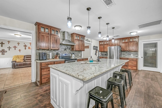 kitchen featuring appliances with stainless steel finishes, a breakfast bar, a spacious island, wall chimney range hood, and hanging light fixtures