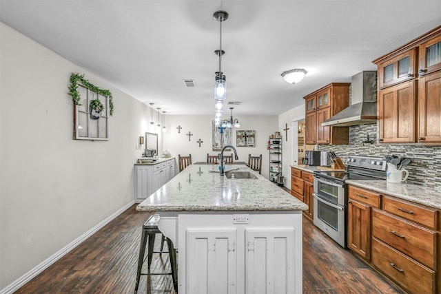 kitchen with a kitchen island with sink, range with two ovens, sink, wall chimney exhaust hood, and light stone countertops