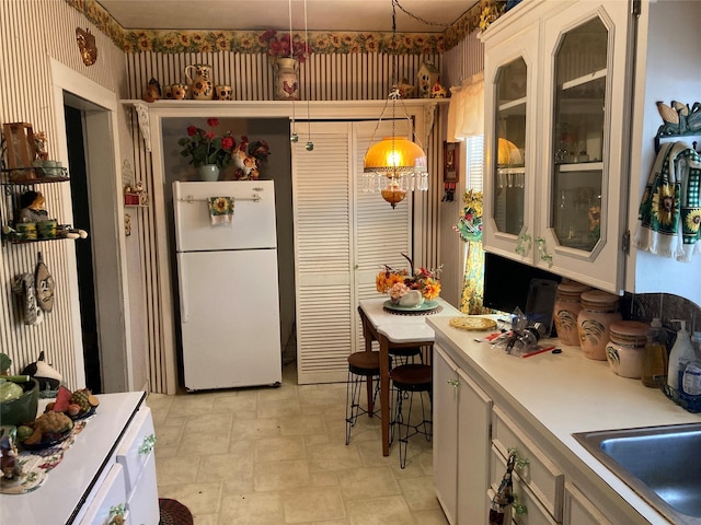 kitchen featuring white cabinets, sink, white fridge, and decorative light fixtures