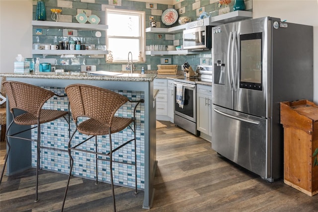 kitchen featuring white cabinetry, light stone countertops, dark hardwood / wood-style floors, a breakfast bar area, and appliances with stainless steel finishes