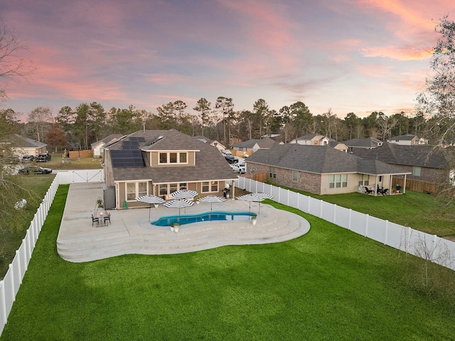 back house at dusk featuring a patio, a lawn, and solar panels