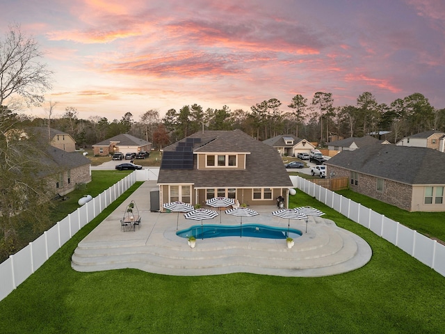 back house at dusk with a lawn, solar panels, a fenced in pool, and a patio