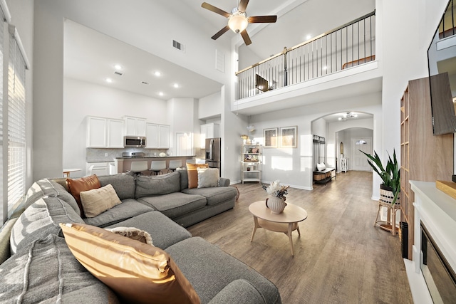 living room with wood-type flooring, a towering ceiling, and ceiling fan