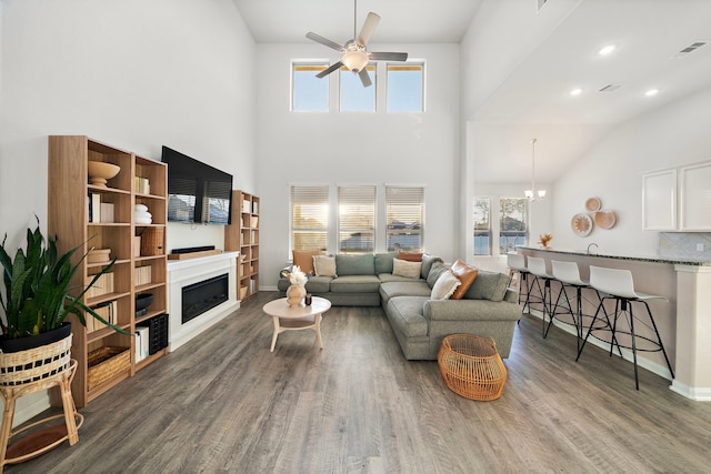 living room with dark hardwood / wood-style flooring, ceiling fan with notable chandelier, and a high ceiling