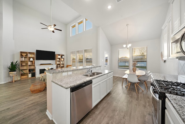 kitchen with an island with sink, sink, white cabinets, hanging light fixtures, and stainless steel appliances