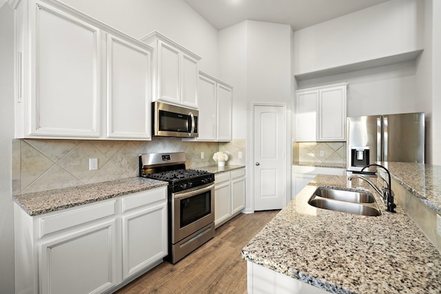 kitchen featuring sink, wood-type flooring, stainless steel appliances, light stone countertops, and white cabinets