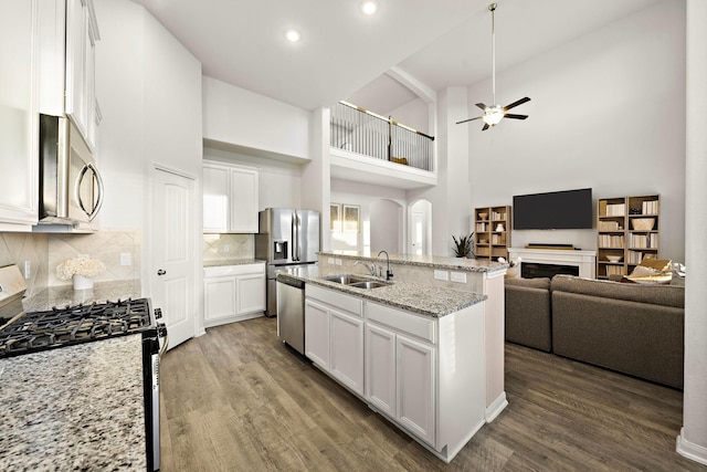 kitchen with sink, appliances with stainless steel finishes, a kitchen island with sink, a high ceiling, and white cabinets