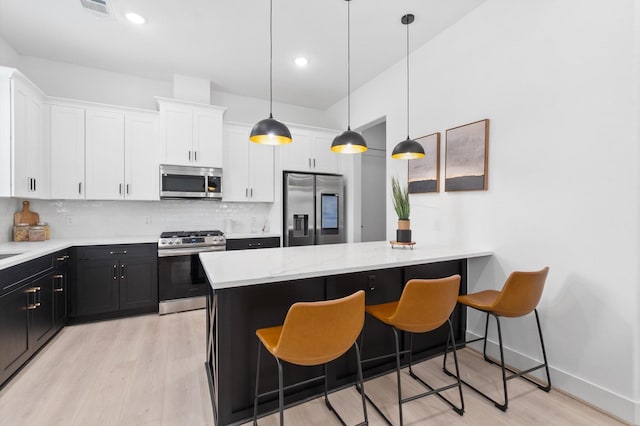 kitchen with appliances with stainless steel finishes, backsplash, a kitchen breakfast bar, white cabinets, and hanging light fixtures