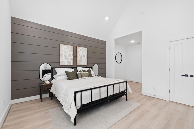 bedroom featuring wooden walls, high vaulted ceiling, and light wood-type flooring